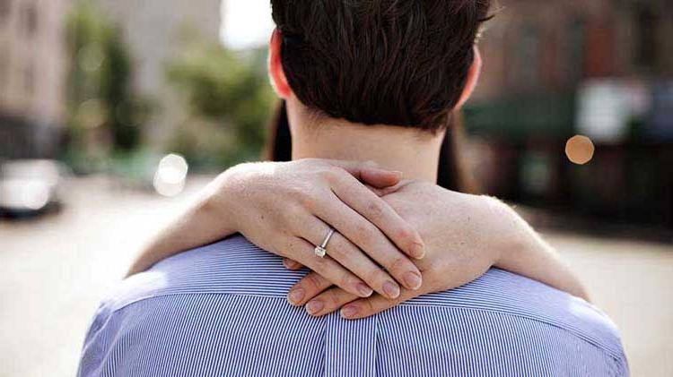 Hands with engagement ring embracing man.