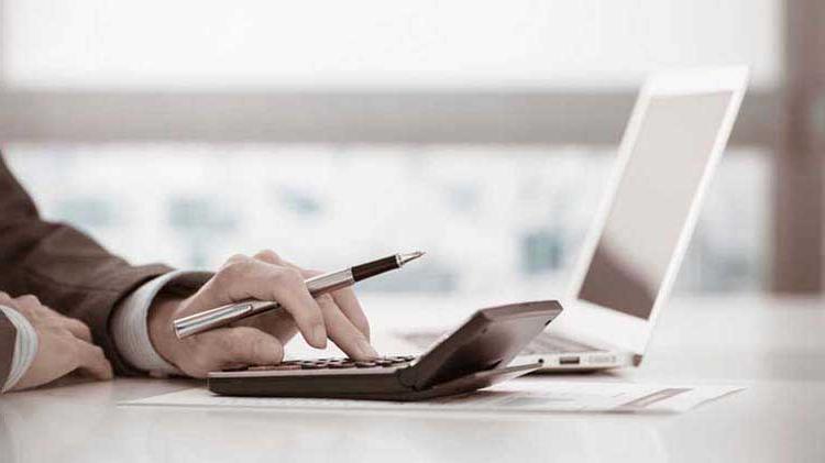 Person's hand operating a calculator next to a laptop