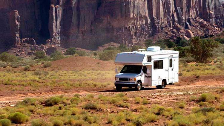 RV on a dirt road with mountains in the background.