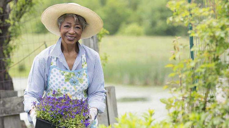 Woman in hat holding plants in garden