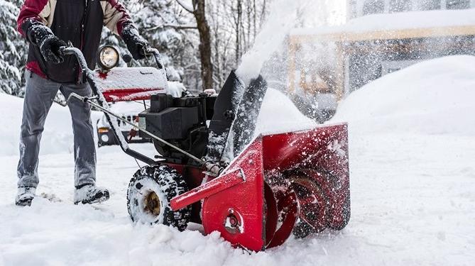 Person walking behind a snowblower as they are clearing the pavement.