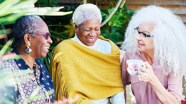 Three women laughing while discussing their retirement and sitting out side drinking coffee.